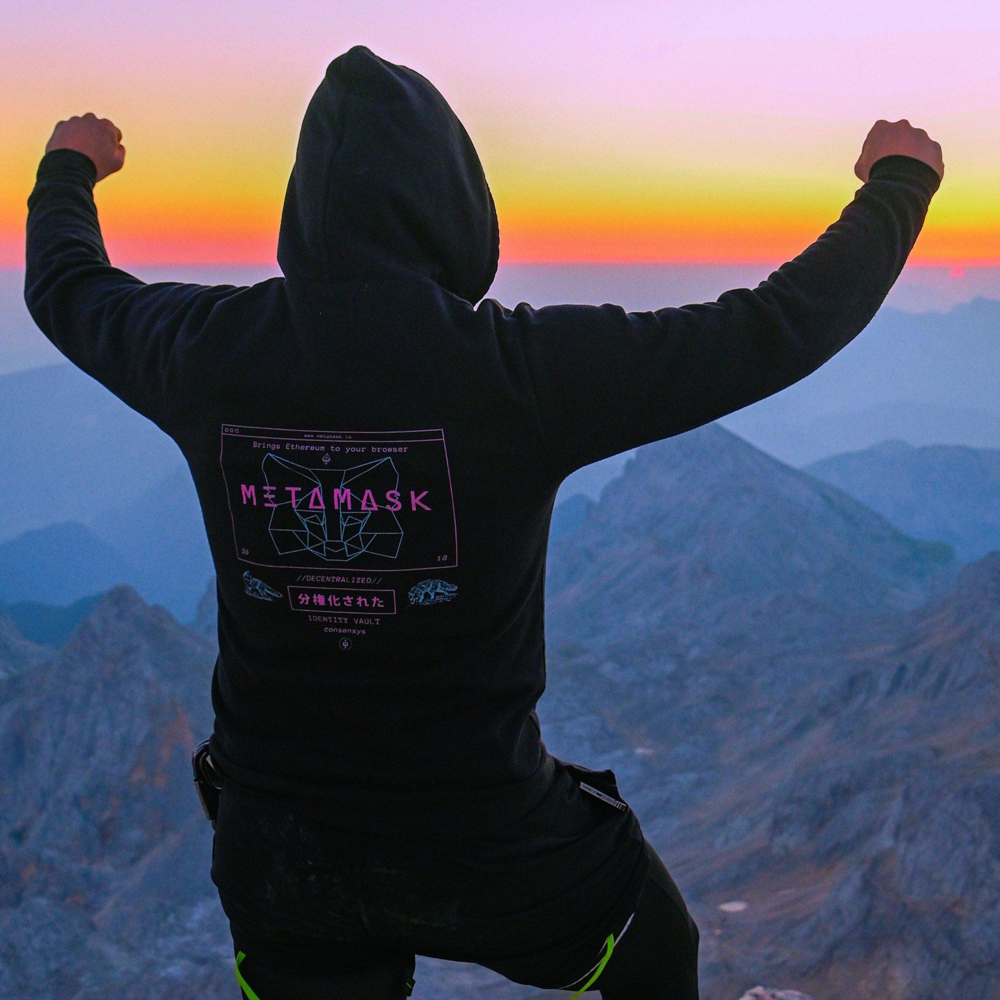 Kristjan on a summit, MetaMask hoodie, sunrise.